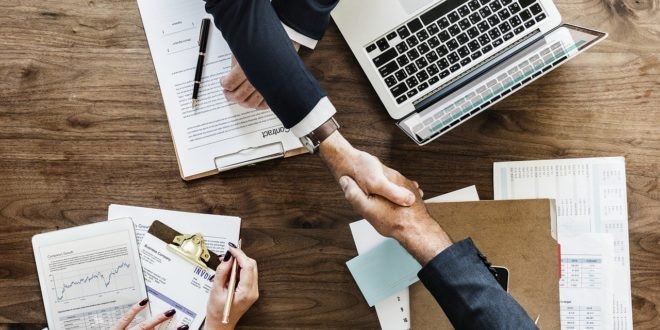 Poignée de main au-dessus d'une table de travail avec plans, contrat et ordinateur